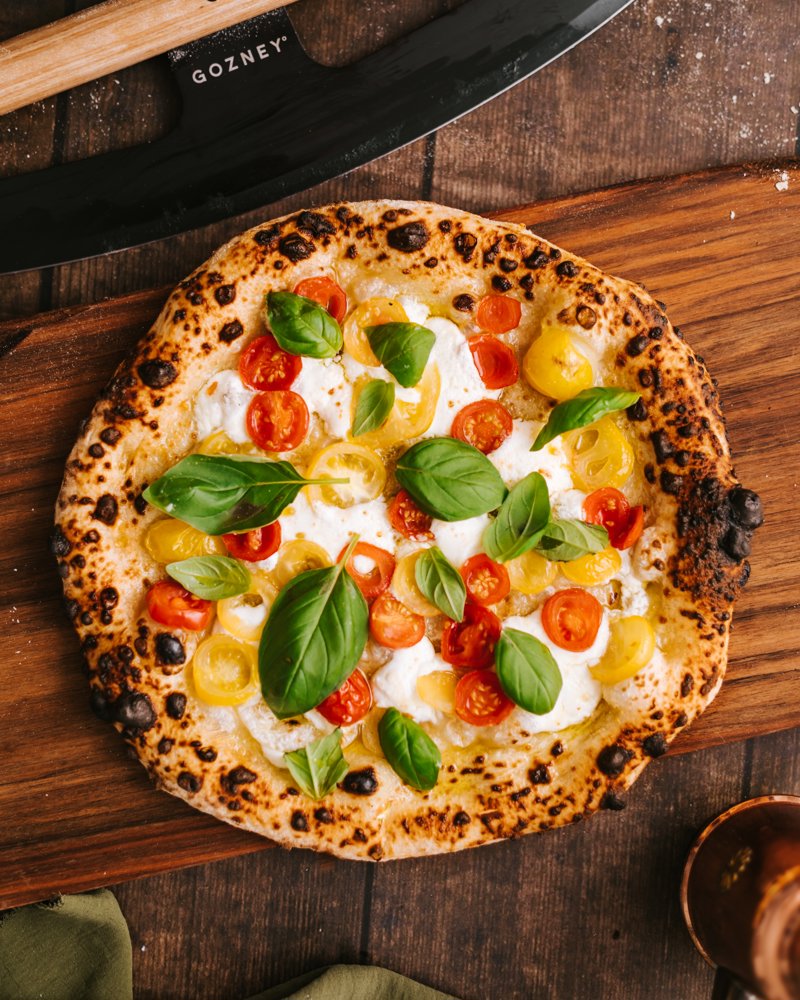 Pizza with red and yellow tomatoes and fresh, basil leaves