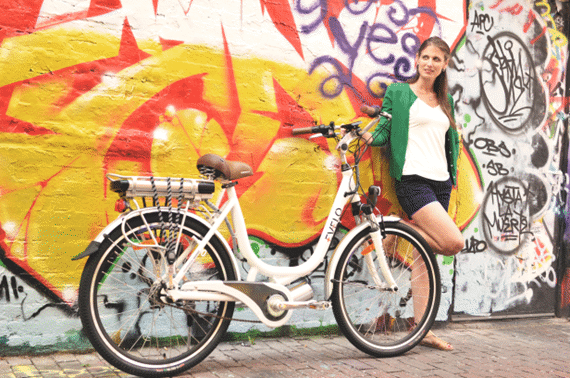 A person standing next to a bicycle who is leaning against the wall of a building painted with graffiti